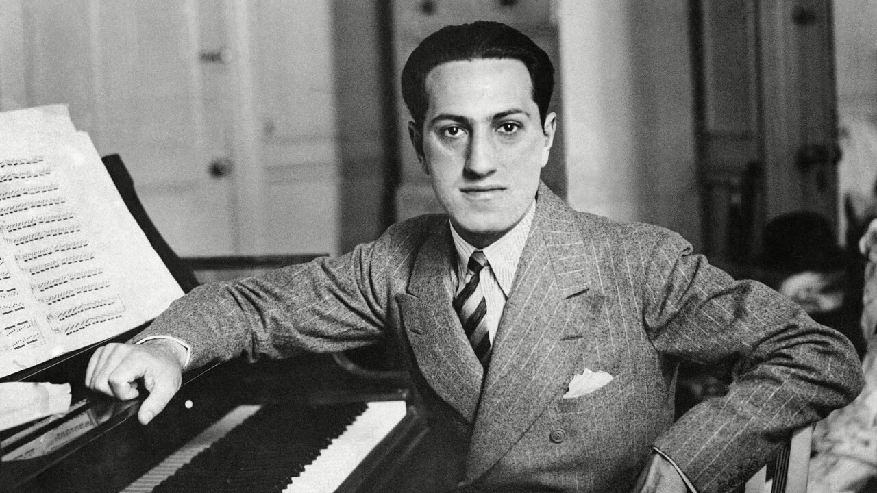 Composer Georges Gershwin seated at the piano, leaning on the music stand.